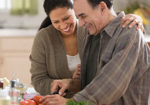 A smiling daughter helps her elderly father prepare a meal