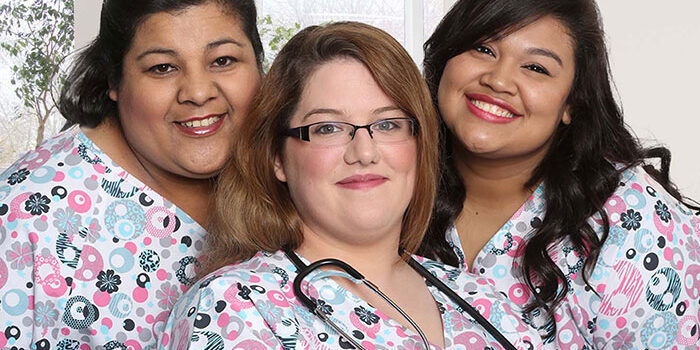 Three smiling caregivers pose on front of a window