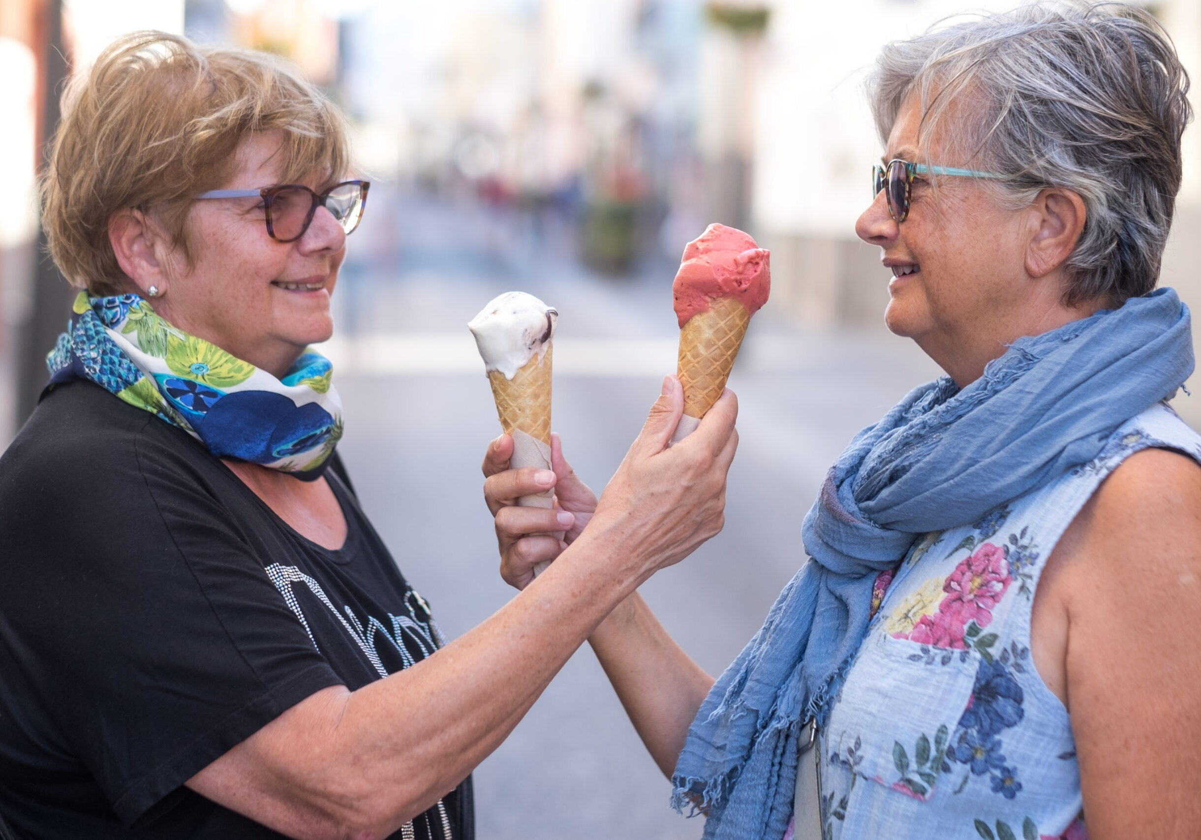 Two elderly women offer each other ice cream cones
